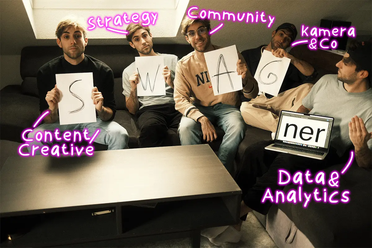 Fünf Personen sitzen auf einer Couch, halten Buchstaben hoch, die das Wort SWAGNER ergeben, und repräsentieren verschiedene Bereiche wie Strategie, Community, Content und Datenanalyse.